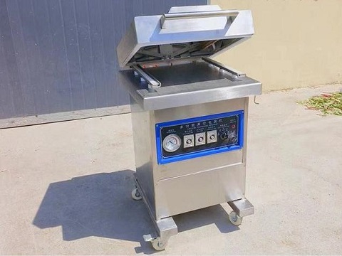Single chamber vacuum sealer sealing a pouch of meat on a stainless steel table