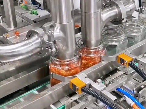 Close-up of an anti-drip filling nozzle dispensing thick sauce into a glass bottle