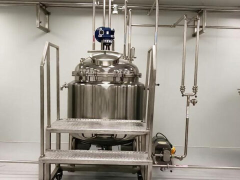 Jacketed stainless steel mixing tank in a food production line with piping and a control panel